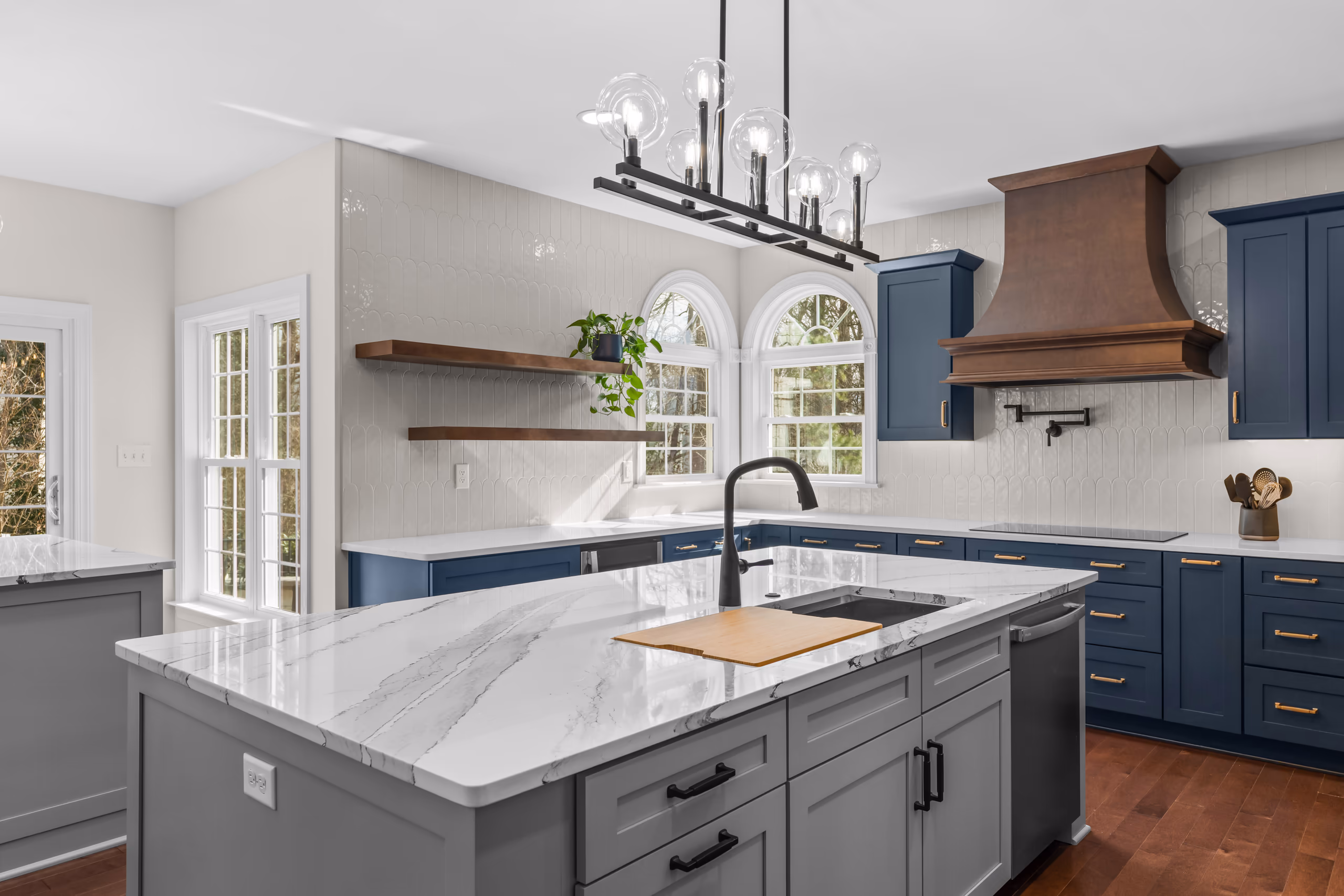 Modern kitchen with navy blue cabinets, white quartz island, and wood range hood.