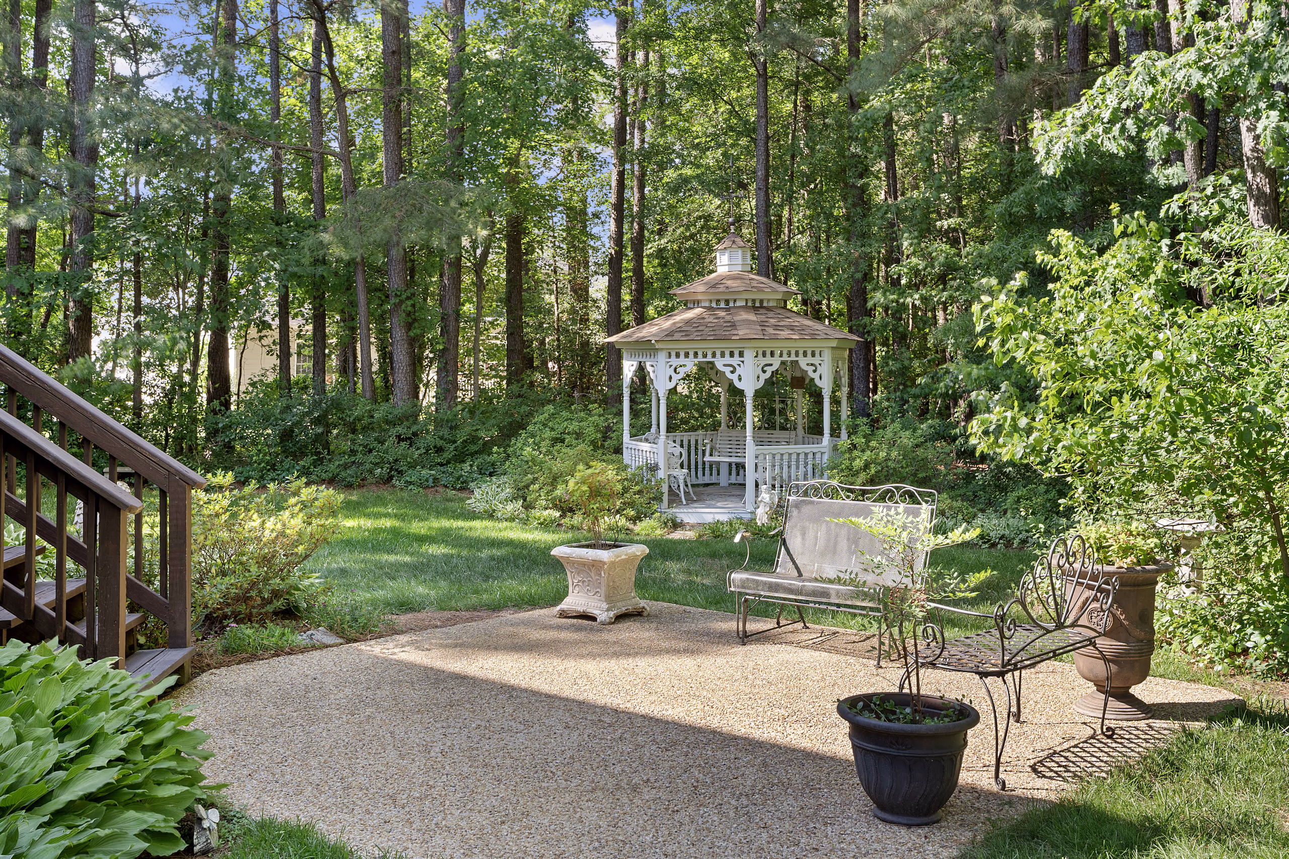 White gazebo in a lush green backyard garden with seating.